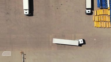 Semi truck with cargo trailer is travelling along a parking lot of a warehouse in the logistics park. A lot of semi-trailers trucks stands at warehouses ramps for load/unload goods. Aerial view