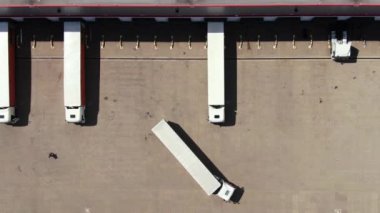 Semi truck with cargo trailer is travelling along a parking lot of a warehouse in the logistics park. A lot of semi-trailers trucks stands at warehouses ramps for load/unload goods. Aerial view