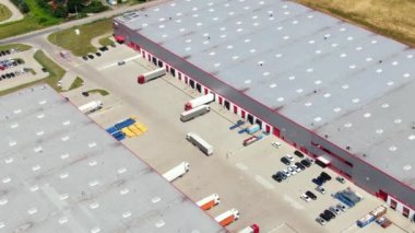 Aerial view of a semi trucks with cargo trailers standing on warehouses ramps for loading/unloading goods on the big logistics park with loading hub