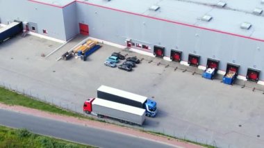 Semi-trailer trucks stand at the ramps of warehouse in the logistics park with loading hub and wait for load and unload goods at sunset. Aerial view