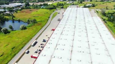 Aerial Shot of Truck with Attached Semi Trailer Leaving Industrial Warehouse/ Storage Building/ Loading Area where Many Trucks Are Loading/ Unloading Merchandise. Shot on Phantom 4K UHD Camera.