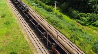 Railway cargo train wagon rides on railroad. Transportation and delivery of cargo in containers. Aerial view over train riding near river and coal power plant.