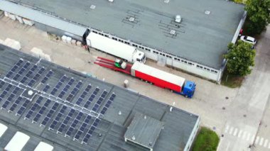 Trucks with semi-trailers stand on the parking lot of the logistics park with loading hub and wait for load and unload goods at warehouse ramps at sunset. Aerial view