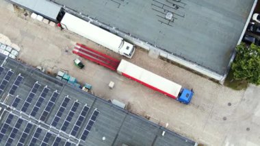 Trucks with semi-trailers stand on the parking lot of the logistics park with loading hub and wait for load and unload goods at warehouse ramps at sunset. Aerial view