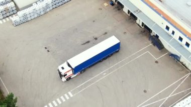 Aerial circling view of a logistics center with warehouse, loading hub with many semi-trailers trucks load/unload goods at sunset