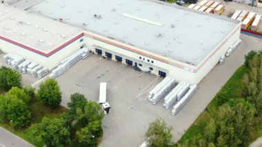 Aerial circling view of a logistics center with warehouse, loading hub with many semi-trailers trucks load/unload goods at sunset