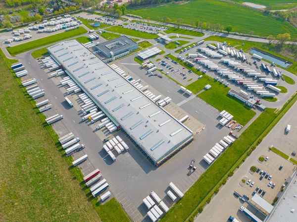 Logistics park with warehouse. Semi-trailers trucks standing on car parking and waiting for loading and unloading goods at ramps. Aerial view