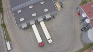 Yarı römorklu kamyonlar lojistik parkının otoparkında durup gün batımında depo rampalarında yükleme ve boşaltma için bekliyorlar. Hava görünümü