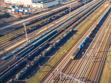 Kargo trenleri. Renkli yük trenlerinin hava manzarası. Tren istasyonunda. Demiryolunda malları olan vagonlar. Ağır endüstri. Trenlerle, şehir binalarıyla ve gün batımında bulutlu gökyüzüyle sanayi manzarası. Üst görünüm