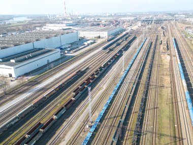 Kargo trenleri. Renkli yük trenlerinin hava manzarası. Tren istasyonunda. Demiryolunda malları olan vagonlar. Ağır endüstri. Trenlerle, şehir binalarıyla ve gün batımında bulutlu gökyüzüyle sanayi manzarası. Üst görünüm