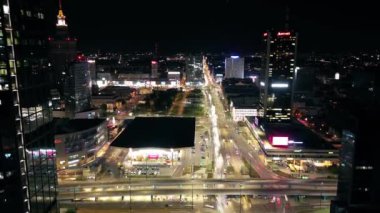 Varşova şehir merkezinin gece vakti hava gözlem insansız hava aracı modern şehir meydanının üzerinde uçuyor, gökdelenler sokakları aydınlatıyor.