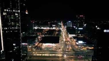 Geceleri Varşova şehir merkezinin hava gözlem insansız hava aracı modern şehir meydanının üzerinde uçuyor, gökdelenler caddeleri aydınlatıyor.