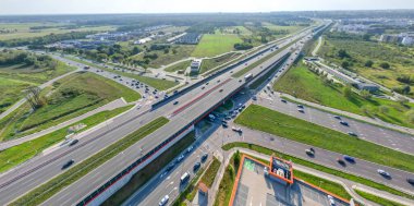 Otoyol kavşağı kavşağının hava manzarası. Yükseltilmiş yolun, trafik kavşaklarının ve yeşil bahçenin drone görüntüsü. Otoyolda giden nakliye kamyonları ve arabalar. Modern şehirde altyapı.