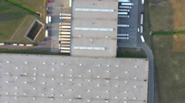 Semi truck with cargo trailer is travelling along a parking lot of a warehouse in the logistics park. A lot of semi-trailers trucks stands at warehouses ramps for load/unload goods. Aerial view