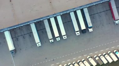 Aerial view of a semi trucks with cargo trailers standing on warehouses ramps for loading/unloading goods on the big logistics park with loading hub
