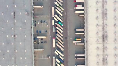 Aerial view of a semi trucks with cargo trailers standing on warehouses ramps for loading/unloading goods on the big logistics park with loading hub