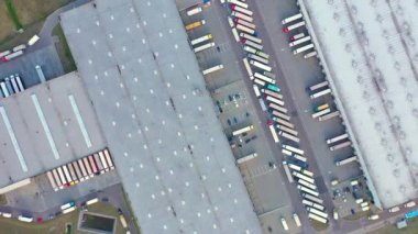 Semi truck with cargo trailer is travelling on a parking lot along a warehouse of a logistics park. Aerial following shot
