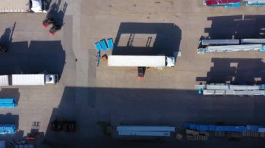 Trucks with semi-trailers stand on the parking lot of the logistics park with loading hub and wait for load and unload goods at warehouse ramps at sunset. Aerial view