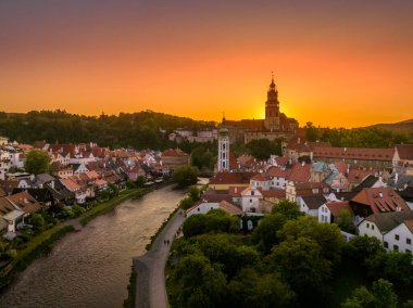 Cesky Krumlov 'un Vltava nehri boyunca St. Jost kilisesi, ortaçağ şatosu ve kırmızı çatılı evleri, çarpıcı renkli dramatik günbatımı gökyüzü
