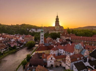 Cesky Krumlov 'un Vltava nehri boyunca St. Jost kilisesi, ortaçağ şatosu ve kırmızı çatılı evleri, çarpıcı renkli dramatik günbatımı gökyüzü