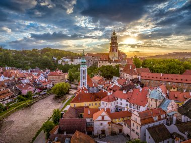 Cesky Krumlov 'un Vltava nehri boyunca St. Jost kilisesi, ortaçağ şatosu ve kırmızı çatılı evleri, çarpıcı renkli dramatik günbatımı gökyüzü