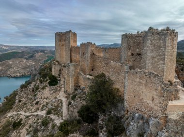 Cortes de Pallas 'taki el Jugar geçidinde bulunan kayalık bir kayanın tepesindeki havadan panoramik manzara, üçgen yerleşim alanı, ok yarıkları, korkuluklar, moa, su tankı, ana kule, dramatik gökyüzü.