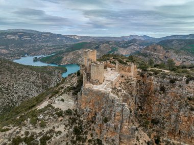 Cortes de Pallas 'taki el Jugar geçidinde bulunan kayalık bir kayanın tepesindeki havadan panoramik manzara, üçgen yerleşim alanı, ok yarıkları, korkuluklar, moa, su tankı, ana kule, dramatik gökyüzü.
