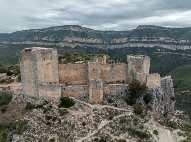 Cortes de Pallas 'taki el Jugar geçidinde bulunan kayalık bir kayanın tepesindeki havadan panoramik manzara, üçgen yerleşim alanı, ok yarıkları, korkuluklar, moa, su tankı, ana kule, dramatik gökyüzü.