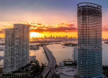 Aerial view of Miami skyline with dramatic colorful sunset sky, MacArthur causeway set between two new real estate development luxury condo building in Florida clipart