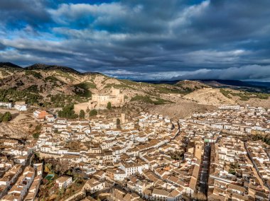 Velez Blanco Kalesi 'nin tepedeki ve kasabadaki havadan görünüşü. Bir ya da iki katlı evler, beyazlatılmış duvarlar ve Endülüs İspanya' sında dramatik bulutlu bir gökyüzü ile döşeli çatılar.
