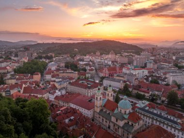 Slovenya 'nın orta kesimindeki tarihi binalar, tepe üstü kırmızı çatı evleri, Slovenya başkentinin günbatımındaki kiliseler ile hava manzarası renkli gökyüzü