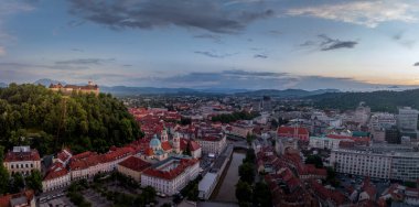 Slovenya 'nın orta kesimindeki tarihi binalar, tepe üstü kırmızı çatı evleri, Slovenya başkentinin günbatımındaki kiliseler ile hava manzarası renkli gökyüzü