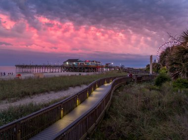 Myrtle Beach boardwalk with Pier 41 restaurant, sand dunes dreamy colorful sunset sky in South Carolina USA clipart