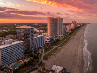 High rise hotels and beach vacation properties line the Carolina coastline on the Atlantic ocean in Myrtle beach popular summer tourist destination stunning colorful sunset sky clipart