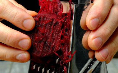 male hands rub on a grater red beet close-up macro