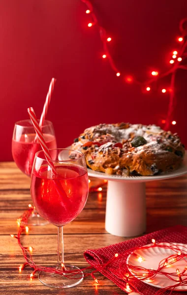 Portuguese Bolo Rei is a traditional Chrismas cake with cocktails and party lights on wooden table