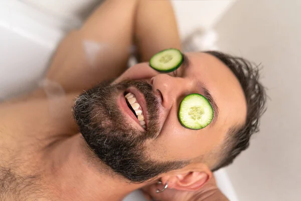 stock image Bearded man with cucumber on front of his eyes relaxing in bath with soapsuds at home