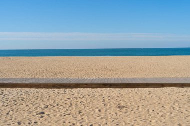 Güneşli bir günde sakin denizin yanındaki kumlu sahilde tahta yol..