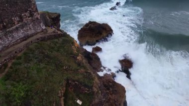 Kayalıklardaki insanların yukarıdan aşağıya hava görüntüsü Portekiz 'in Nazare kasabasındaki Kuzey Sahili' ndeki büyük dalgaları izliyor.