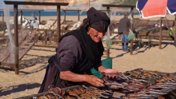 2022年12月9日 葡萄牙纳扎尔市 身穿黑色衣服的老妇人在大西洋沿岸渔民村的海滩上出售干鱼 — 图库视频影像