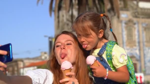 舌を示すアイスクリームを持つ幸せな若い母親と小さな娘と路上で電話で写真を撮る — ストック動画