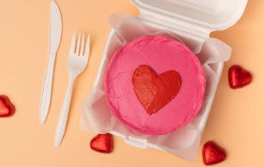 Valentine day bento cake In eco box with knife and fork on beige background, sweet dessert surprise gift for Valentines day, top view.