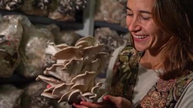 happy young woman sniffing flowers when holding mushrooms against the oyster mushroom farm.