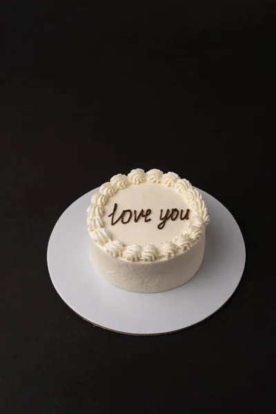 Small white cake with black text love you on the black background. Minimalistic style