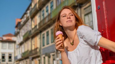 Young adult red haired woman enjoying ice cream and sunshine in the town