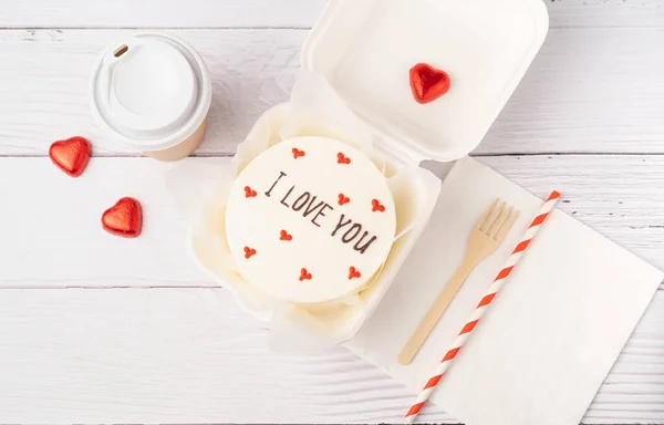Bento cake with text I love you, on white wooden planks background. Korean style cakes in a box for one person and coffee cup. Flat lay