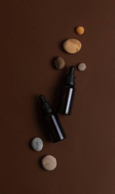 İki şişe koyu kehribar rengi cam, esaslı yağ ve deniz taşları, güzel kahverengi arka planda.