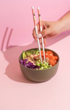 Hawaii balık somonu kasesinin üzerinde pembe arka planda çubukları olan eller. sert gölgeler, minimalizm