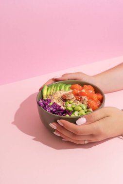 Havai balık somon kasesini pembe arka planda tutan Wonan elleri. sert gölgeler