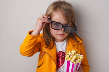 Tatlı patlamış mısır ve sinema gözlükleriyle kameraya bakan tatlı küçük kız.